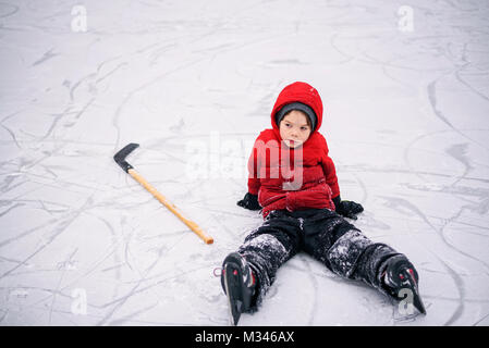 Junge sitzt auf Eis mit seiner hockey stick Stockfoto