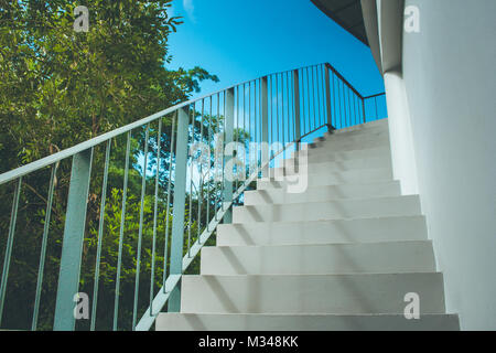 Vorderansicht in der Nähe von Leer weißer Beton Treppe und Geländer aus Metall an der Außenseite von Gebäuden mit blauem Himmel Hintergrund im Vintage Style. Stockfoto
