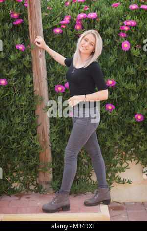 Schöne blonde Mädchen in Jeans durch eine Wand von Blumen stand Stockfoto