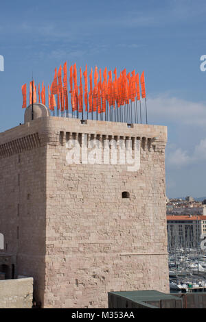 Orange Flaggen im Wind flattern auf einem steinernen Turm im Museum für Europäische und mediterrane Kulturen komplex in Marseille, Frankreich. Stockfoto