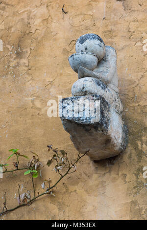 Ein einfacher Stein Skulptur einer Person das Trinken aus einer Schüssel. Die Skulptur ist auf der Seite eines tan Stuck Wand. Schüssel Stockfoto