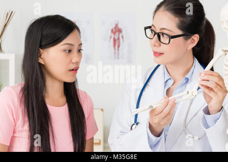 Attraktive Schönheit Mädchen Patienten fragen Problem beim Arzt über menschliche Skelett Modell Krankheit erklären und empfohlene Behandlung Lösung bieten. Stockfoto