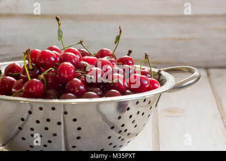 Metall Sieb voller frisch Kirschen über eine rustikale Board. Kirsche. Stockfoto