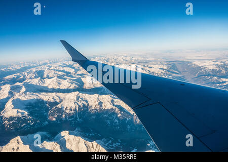 Auf der Suche durch das Fenster Flugzeuge während des Fluges eine verschneite Italien und Osterreich Alpen mit blauer Himmel ohne Wolken. Stockfoto