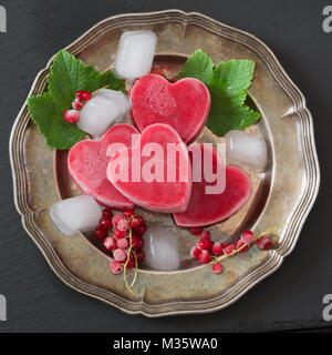 Hausgemachtes Eis in Form der Herzen. Rote Johannisbeere Limonade garniert Minze und Eis auf vintage Gericht und schwarzen Hintergrund. Ansicht von oben. Frozen Drinks. Stockfoto
