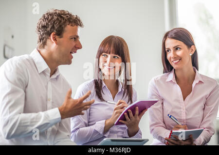 Junge Unternehmer erklären, während die weiblichen Kollegen schreiben in Bücher im Büro Stockfoto