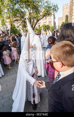 Büßer Kind der Bruderschaft des "La Paz" geben einen kleinen Stempel zu einem Kind der Öffentlichkeit. Stockfoto