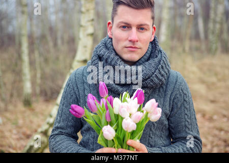 Portrait von gutaussehenden blonden Mann im Freien mit Tulpen Stockfoto