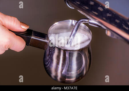 Woman's Hand mit einem Edelstahl milchaufschäumung Krug, unter Dampf-/Dämpfen Zauberstab der eine gewerbliche Espressomaschine, Schaum zu erzeugen. UK. Stockfoto