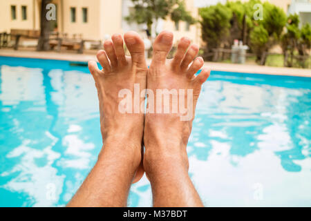 Junger Mann entspannende nex zum Pool. In der Nähe der Beine eines Mannes. Stockfoto