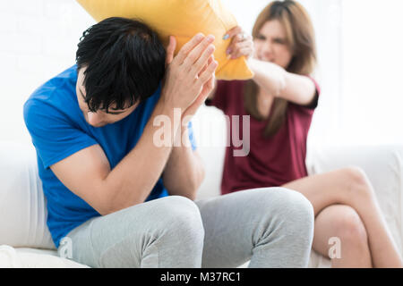 Junges Paar Streit ling emotional zu Hause, Frau mit einem Kissen angreift, man ist verwirrt, argumentieren auf Familie Haushalt. Probleme in der Familie Konzept Stockfoto