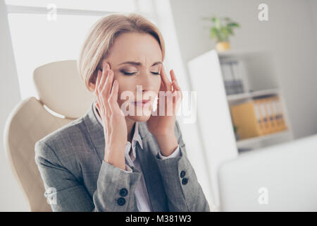 Hübsche, attraktive, Reife, Erwachsene mittleren Alters Frau im klassischen Outfit sitzt auf einem Sessel am Arbeitsplatz, Workstation, Tempel mit den Fingern berühren. Stockfoto