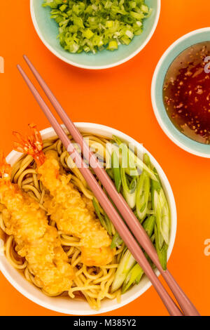 Im japanischen Stil Tiger Garnelen Tempura Nudelsuppe mit Frühlingszwiebeln gegen einen orangen Hintergrund Stockfoto