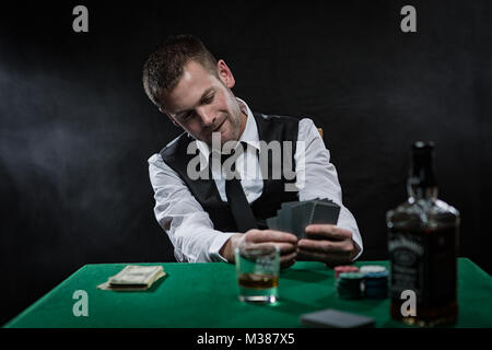 Harter Kerl, der seine Pokerkarten nahe an seiner Brust am Pokertisch spielt Stockfoto