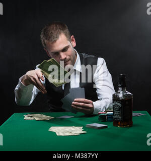 Harter Kerl spielen seine Karten in der Nähe von seiner Brust am Pokertisch Stockfoto