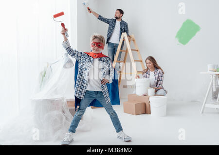 Familie ihr Haus renovieren und Malerei Mauern, der Junge trägt ein Superheld Kostüm und Halten einer Rolle Stockfoto