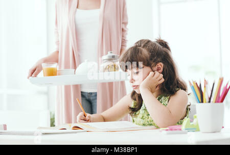 Süße Mädchen studieren zu Hause, ihre Mutter bringt ihr einige gesunde Snacks, Familie und Lifestyle Konzept Stockfoto