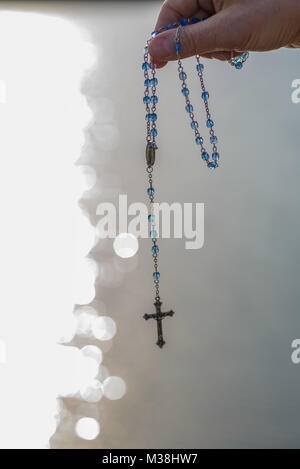 Nahaufnahme der Hand einer Frau mit einem Rosenkranz entlang der Küste bei Sonnenuntergang Stockfoto