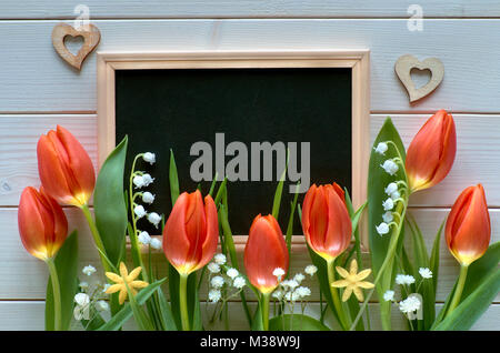 Ostern Zusammensetzung mit Blackboard mit Frühling Blumen, Tulpen und Maiglöckchen eingerahmt. Platz für Ihren Text auf der Tafel. Stockfoto