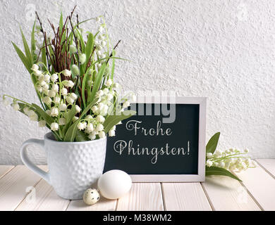 Ostern Zusammensetzung mit Blackboard mit Keramik Henne, Eier dekoriert und und Maiglöckchen Blumen. Caption "Happy Frohe Phingsten' bedeutet 'Penteco Stockfoto