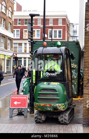 Männer an der Arbeit an einer belebten London oder innerstädtischen Straße graben ein Loch in der Straße mit Bobcat oder Mini Bagger mit Diversion Gehweg für Fußgänger Stockfoto