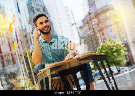 Positiver Mann seinem Freund telefonieren und ihn aufforderte, Kaffee zu trinken zusammen Stockfoto