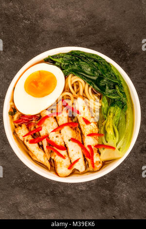 Im japanischen Stil Huhn und Chili Ramen Suppe oder Brühe mit Pak Choi gegen einen schwarzen Tischplatte Stockfoto