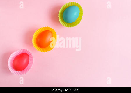 Ostern Hintergrund. Flach drei bunt bemalte Eier in Rosa geschnitzte cupcakes Formen sind diadonally liegen auf einem rosa Hintergrund mit kopieren. Stockfoto