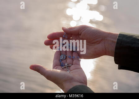 Frau mit einem Rosenkranz in den Händen beten vor der See bei Sonnenuntergang Stockfoto