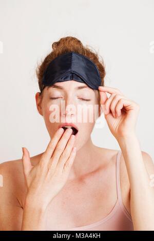 MODEL RELEASED. Junge Frau müde Gähnen aus Mangel an Schlaf tragen eine Schlafbrille. Stockfoto