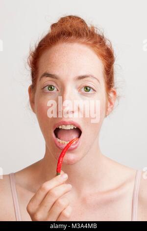 MODEL RELEASED. Frau mit roten Chili vor Ihrem offenen Mund. Stockfoto