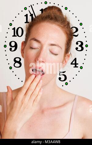 MODEL RELEASED. Junge, müde Frau Gähnen und über ihren Mund mit Uhr im Hintergrund. Stockfoto