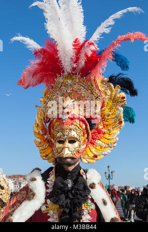 Venedig, Venetien, Italien, 10. Februar 2018. Bunte Kostüme beim Karneval in Venedig an einem sonnigen Tag am letzten Wochenende des Festivals. Mann mit einem aufwendigen Maske mit Federn schließen sich gegen einen blauen Himmel. Stockfoto