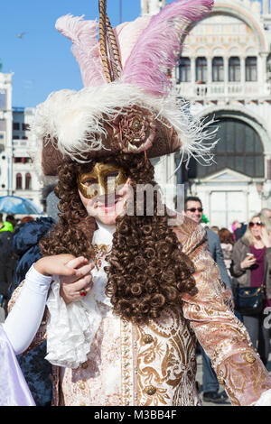 Venedig, Venetien, Italien, 10. Februar 2018. Bunte Kostüme beim Karneval in Venedig an einem sonnigen Tag am letzten Wochenende des Festivals. Glücklich lächelnde Mann in Piazzetta San Marco mit der Basilika San Marco. Stockfoto