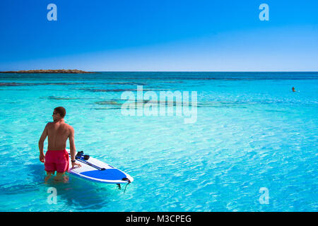 Tropischen Sandstrand mit türkisfarbenem Wasser, in Elafonisi, Kreta, Griechenland. Ein junger Mann mit Surf sup Board Stockfoto
