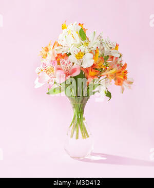 Blumenstrauß von Alstroemeria in einem durchsichtigen Glas Vase auf rosa Hintergrund Stockfoto