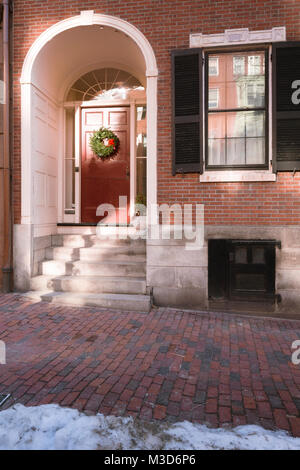 A Christmas Wreath auf einer roten Tür in der Gegend von Beacon Hill, Boston, Massachusetts. Stockfoto