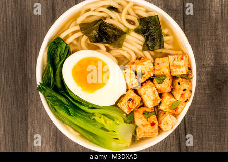 Im japanischen Stil vegetarisch Tofu Nudeln Ramen Suppe oder Brühe auf einem dunklen Holztisch Top Stockfoto