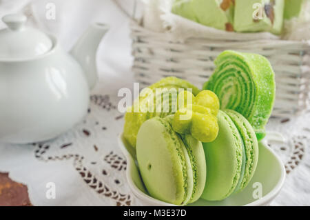 Frisch gebackene farbige Makronen in Weidenkorb mit Griffen mit kleinen weißen Blüten auf Holz- Hintergrund. Selektive konzentrieren. Stockfoto