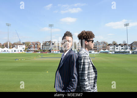 Zwei schöne Doppel-/Mixed Race Jungs tragen maßgeschneiderte Anzüge um eine Cricket Ground sind Wandern - Es ist ein heller Tag, Es gibt Häuser im Hintergrund Stockfoto