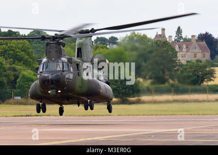 Boeing CH-47 CH-147 Chinook schweben mit dem Taxi auf der RAF Fairford in den Cotswolds. Eine CH-47F CH-147F-Variante, mit Cotswolds Landhaus darüber hinaus Stockfoto