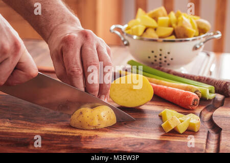 Häckseln Kartoffeln für hausgemachte Huhn und weiße Bohnensuppe. Zutaten gehören Kartoffeln, Karotten und Sellerie. Stockfoto