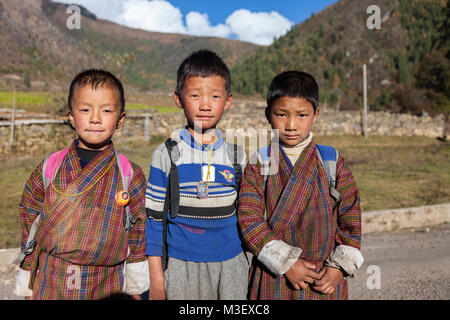 Phobjikha, Bhutan. Kikorthang Dorf. Drei Schuljungen, zwei tragen traditionelle Gho, einer in westliche Kleidung. Stockfoto