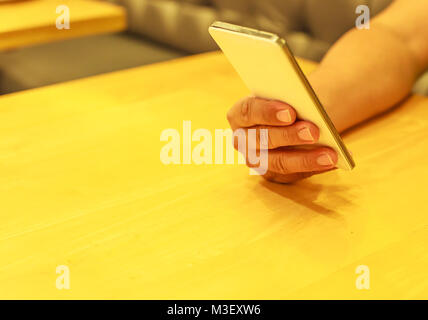 Hand und unter Verwendung von Smart Handy auf dem Tisch indoor Stockfoto