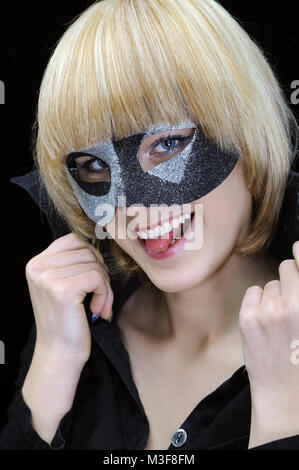 Closeup Portrait von jungen fröhliche Frau mit herausgestreckter Zunge mit Maskerade auf schwarzem Hintergrund Stockfoto
