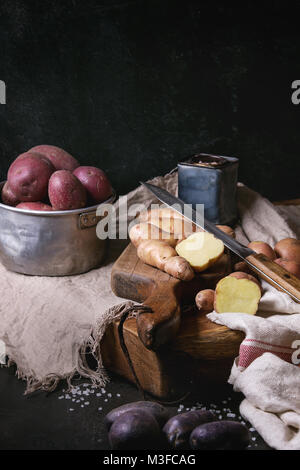 Vielzahl von Roh ungekocht Biokartoffeln unterschiedlicher Art und Farben Rot, Gelb, Lila auf Holz Schneidebrett mit Küche Handtücher über schwarze Tabelle. D Stockfoto