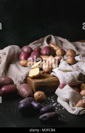 Vielzahl von Roh ungekocht Biokartoffeln unterschiedlicher Art und Farben Rot, Gelb, Lila auf Holz Schneidebrett mit Küche Handtücher über schwarze Tabelle. D Stockfoto
