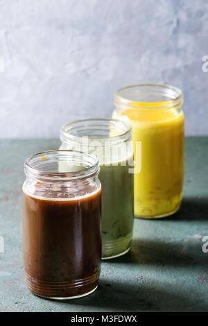 Vielzahl von bunten Iced Latte Getränke. Eiskaffee, Kurkuma und Matcha Latte Cocktails in Gläsern über Grau Grün Textur Hintergrund. Platz kopieren Stockfoto