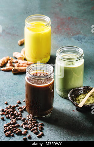 Vielzahl von bunten Iced Latte Getränke. Eiskaffee, Kurkuma und Matcha Latte Cocktails in Gläsern mit Zutaten oben über Grau Grün Textur b Stockfoto