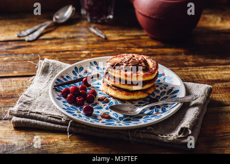 Quark Pfannkuchen mit Haselnusspaste, gefroren Cherry und Vanilla Pod. Teekanne mit Löffeln und Glas von Beeren für den Hintergrund. Stockfoto